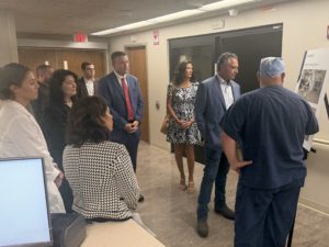 Group of professionals in a hallway looking at a large poster board mounted on the wall in what appears to be an office or medical building.
