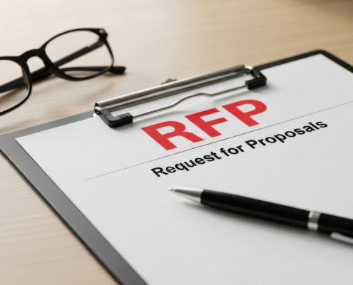 Clipboard with an RFP document reading 'RFP' and 'Request for Proposals' beside a pair of eyeglasses and a pen on a wooden desk.