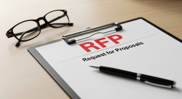 Clipboard with an RFP document reading 'RFP' and 'Request for Proposals' beside a pair of eyeglasses and a pen on a wooden desk.